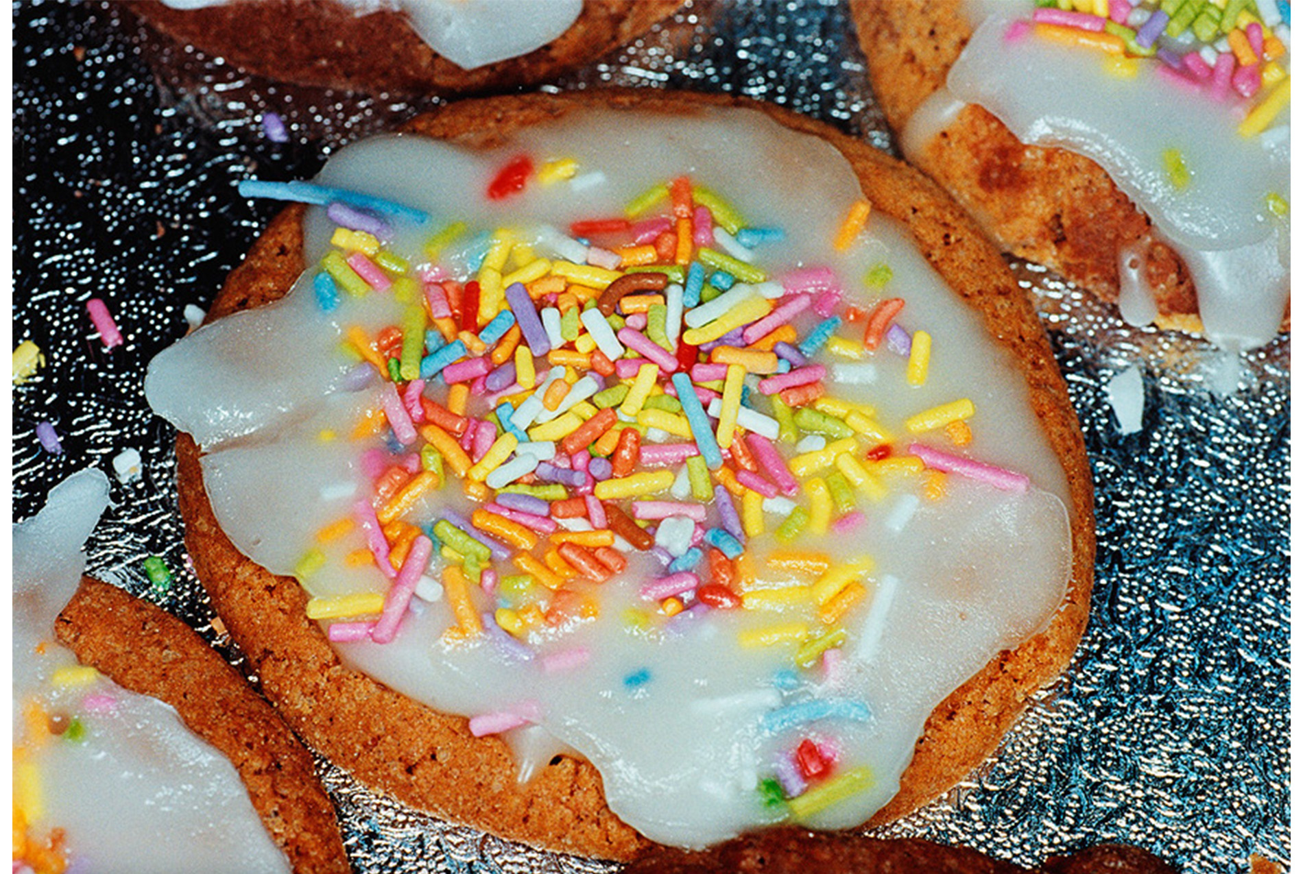 close-up, pressed metal patterned surface holding large flat cookies with white frosting and sprinkles
