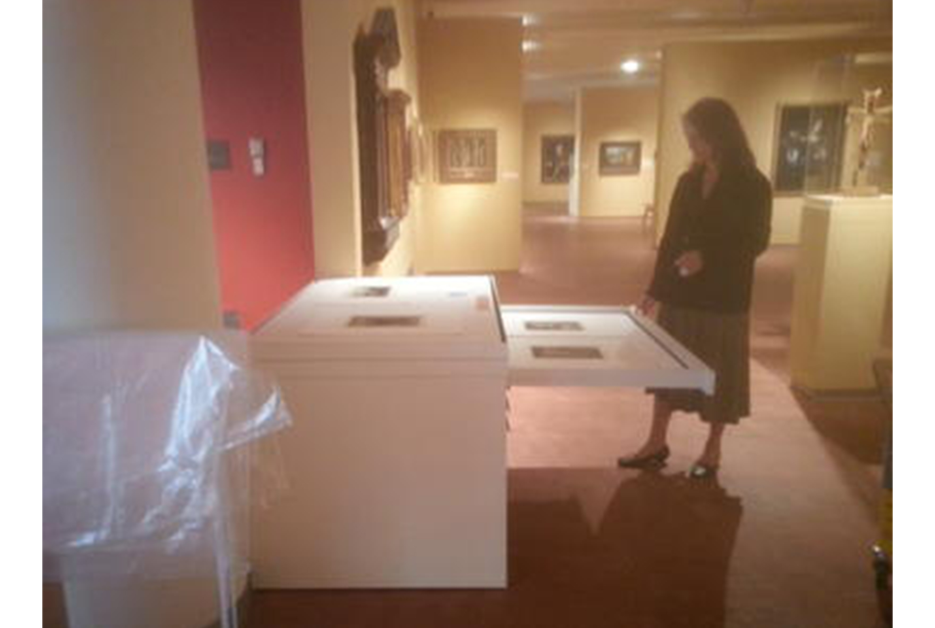 woman stands in an art gallery looking at a white cabinet with one of its drawers pulled upon