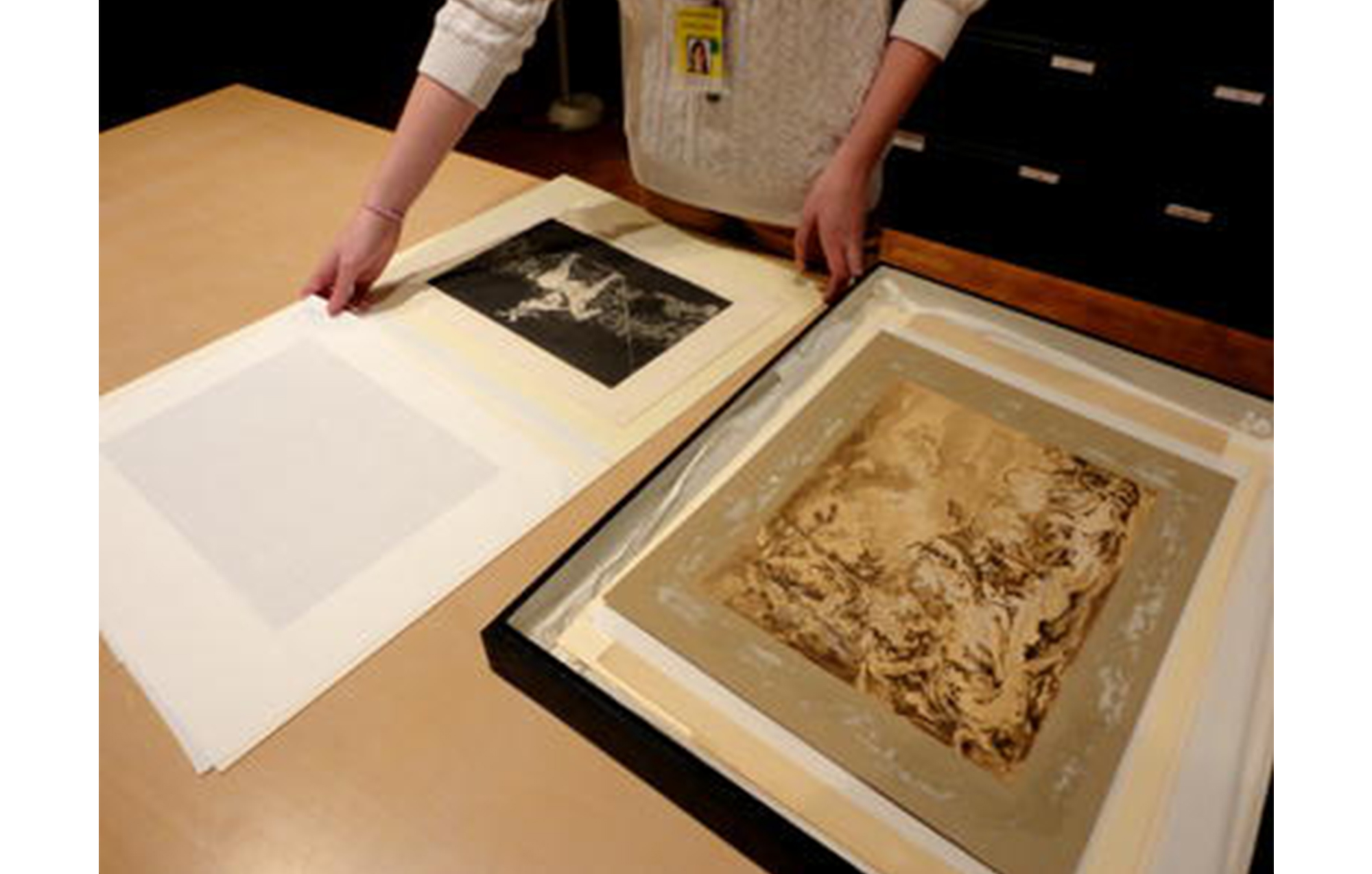 table with a large print spread out across it and a girl holding the edges of the print