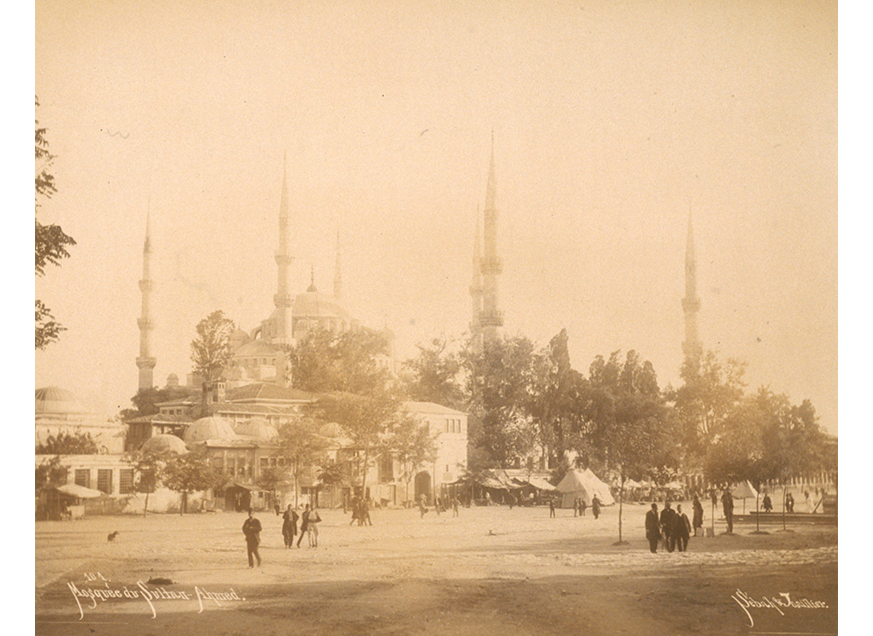 photograph of a large building (Sultan Ahmet Mosque in Istanbul) with a field in front of it and people walking around