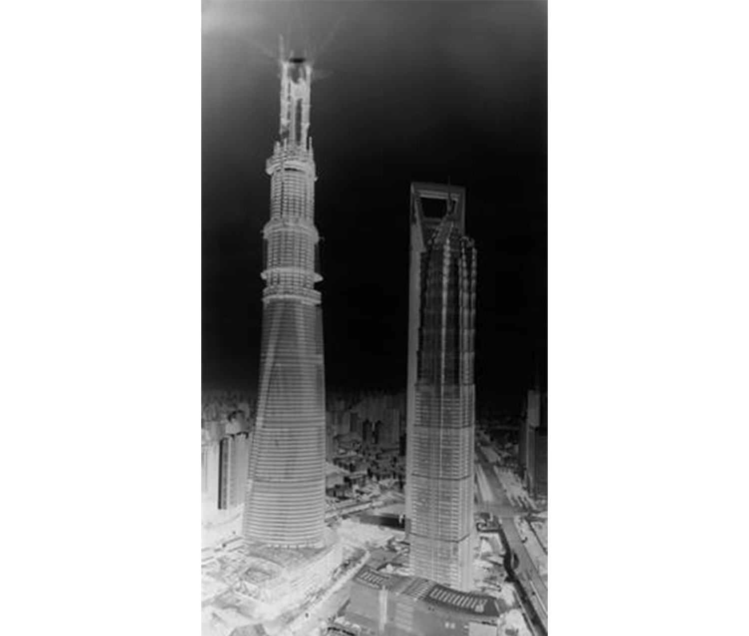 inverted black and white image of a tower standing high above other buildings in a city, against a night sky