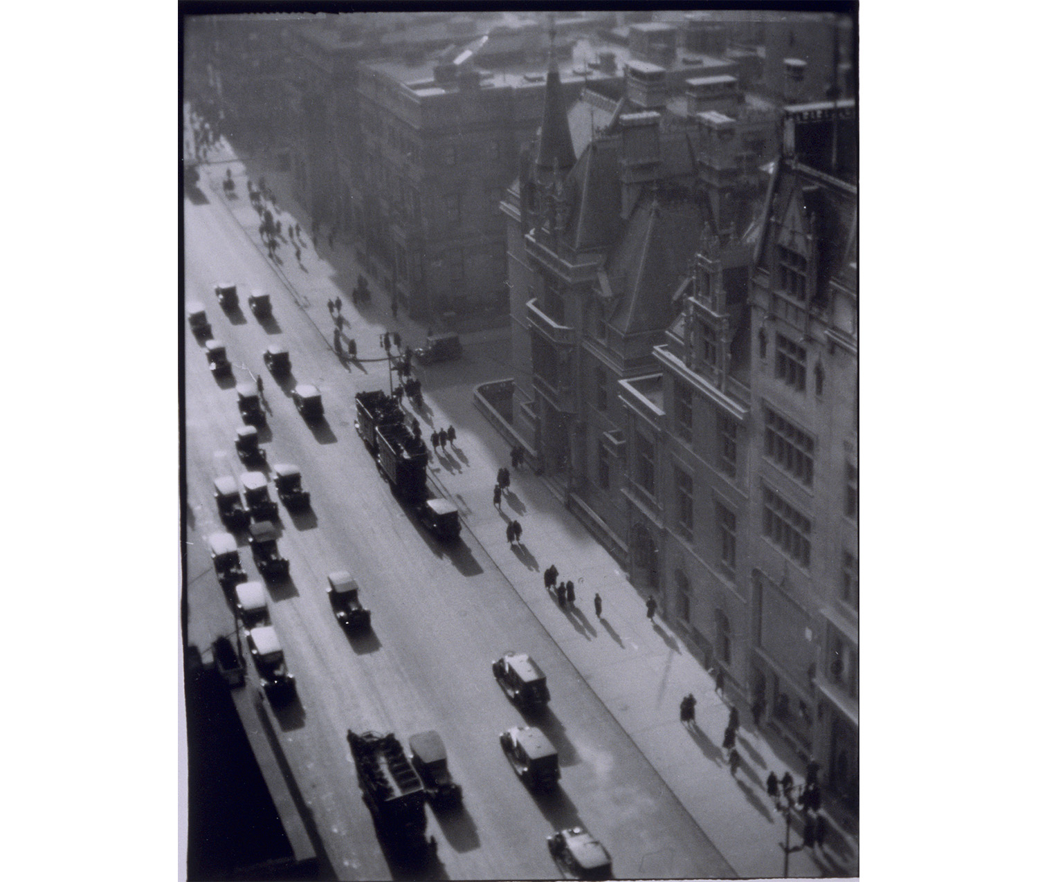 view from above of a city street, with cars driving and people walking on the sidewalks