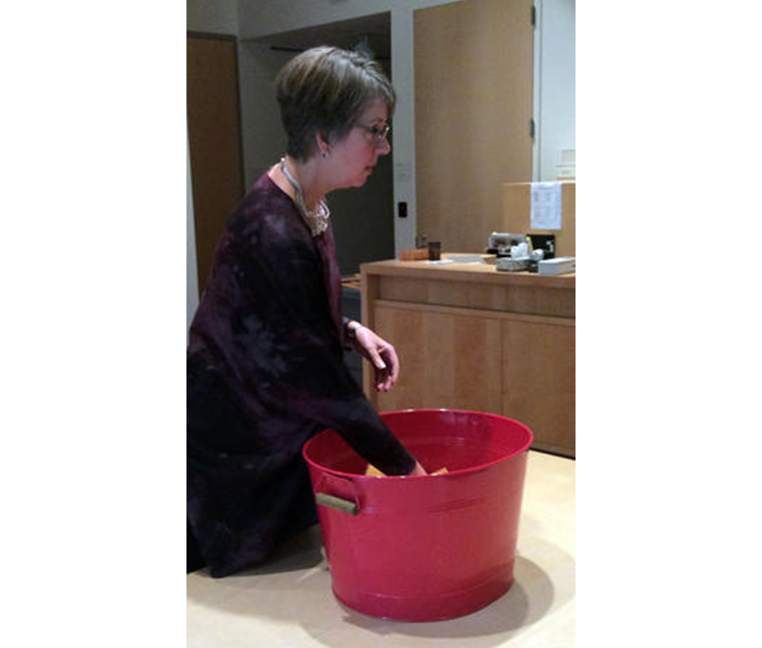 woman reaching her hand into a large red bucket full of multicolored slips of paper