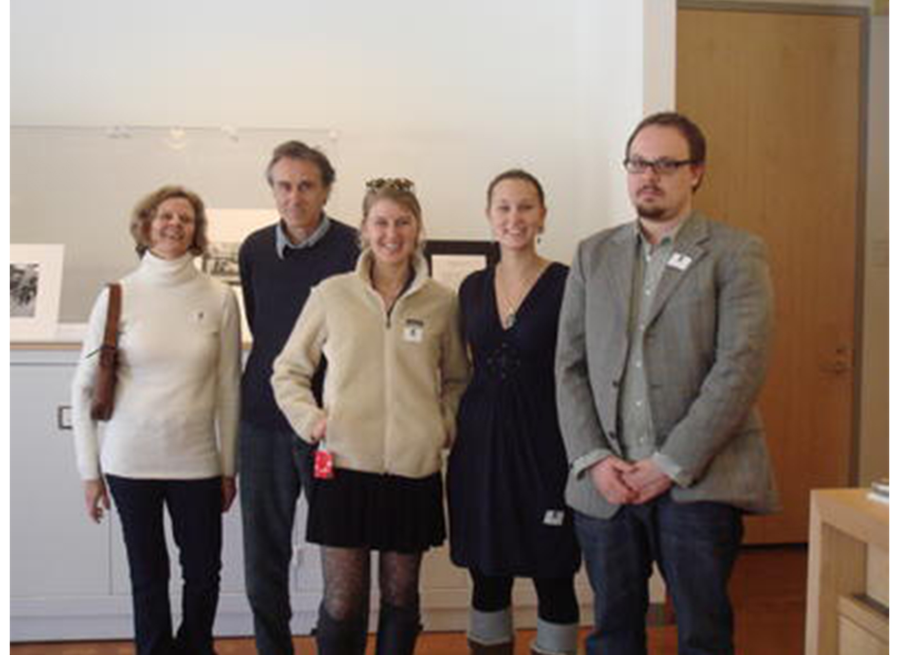 five people stand in front of a display of prints, dressed in formal clothing and smiling