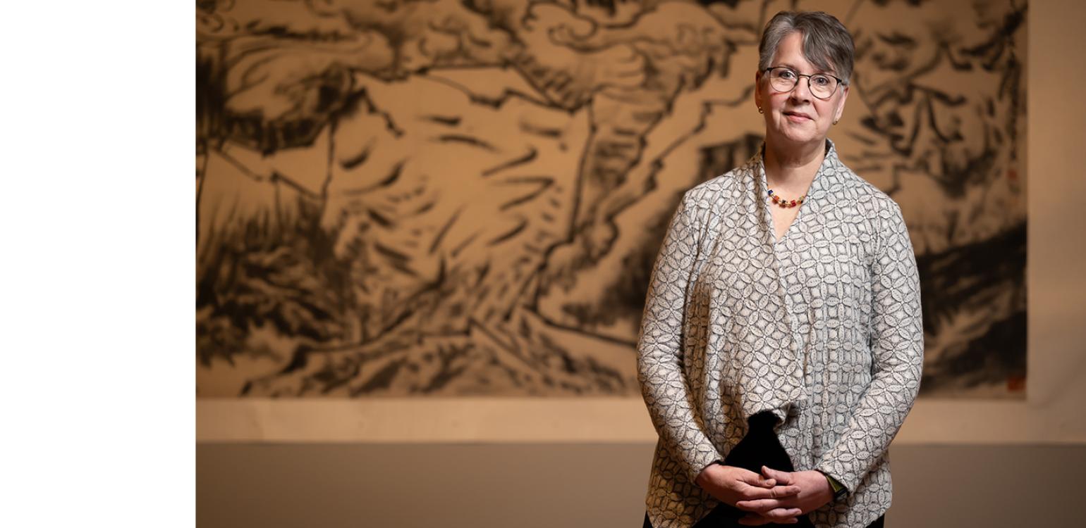 Photo of a woman with short hair standing in front of a calligraphic painting 