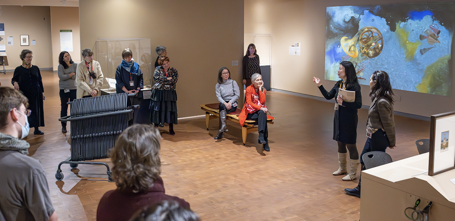 Gallery full of people circled around two people presenting information