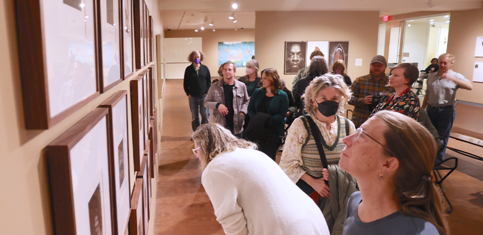 Gallery of a dozen or so people in a gallery looking at artwork 