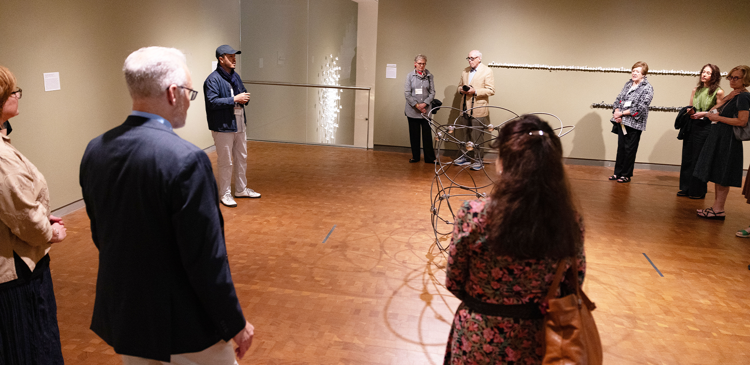 Ten people gathered in a circle in an art gallery listening to a person speak about the art
