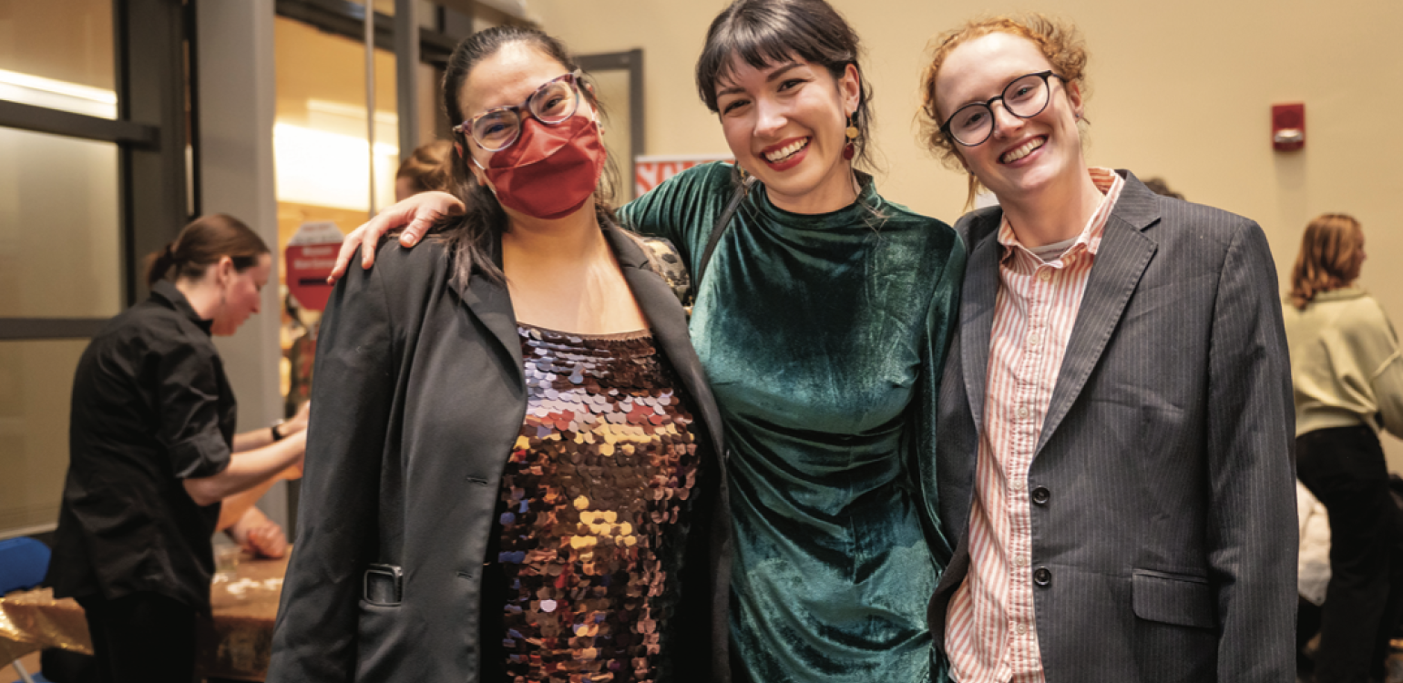 Three students dressed in dresses and sport jackets and posing in a row with arms around one another