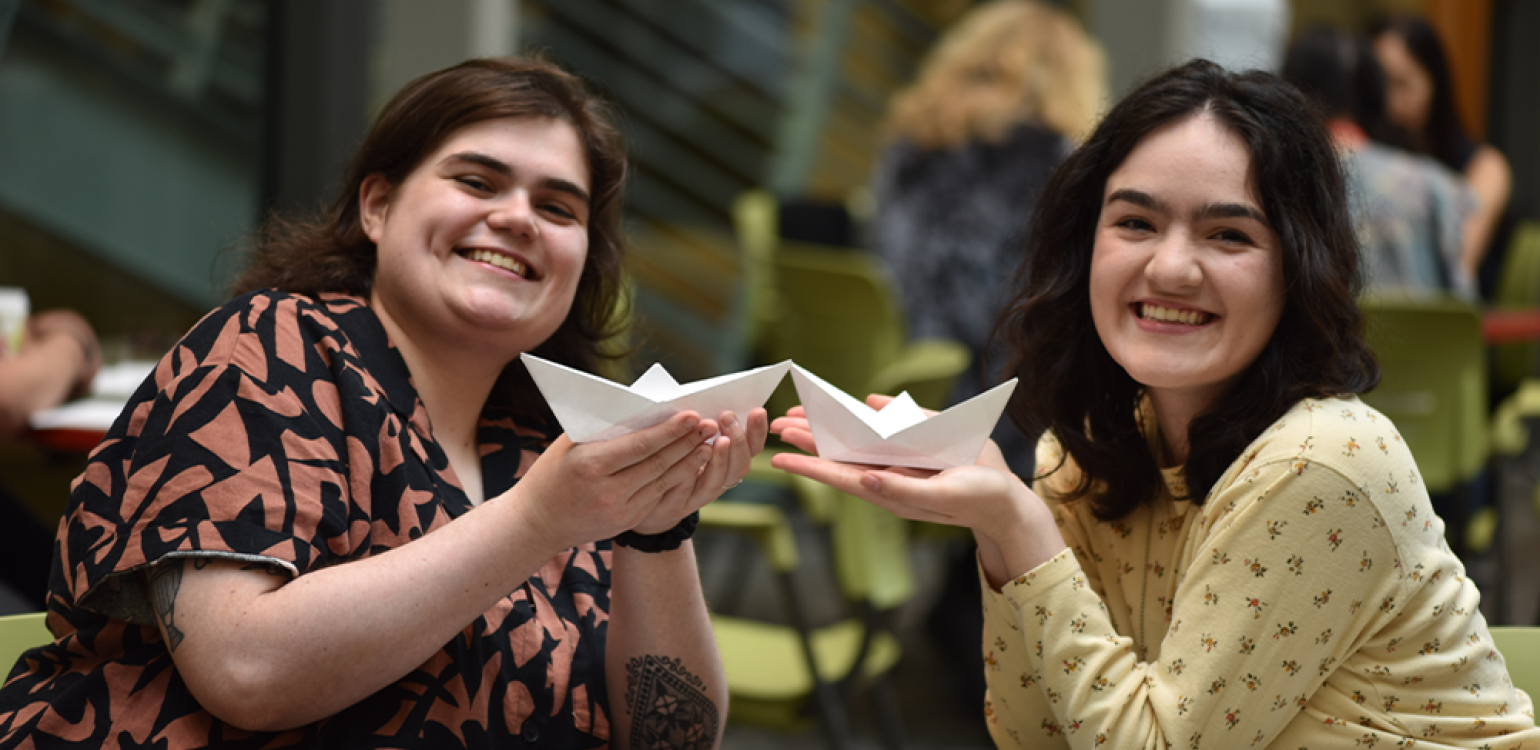 Two people holding up and displaying origami paper boats and smiling 