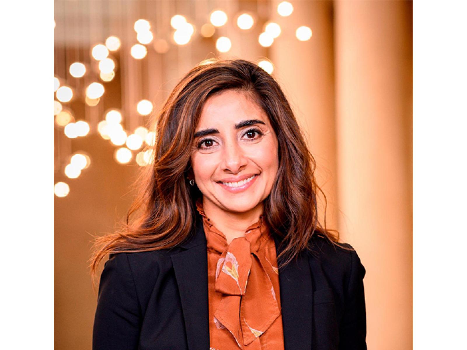 Headshot of Asma Naeem, she is smiling and wearing an orange blouse and black blazer.