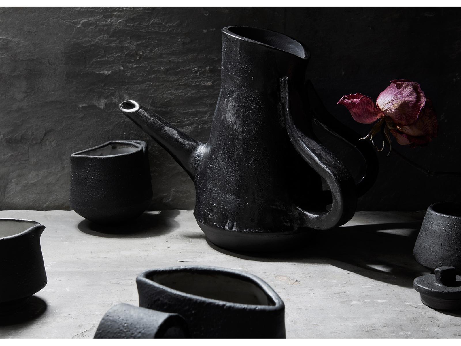 Black glazed tea set on white table with black background and a purple flower