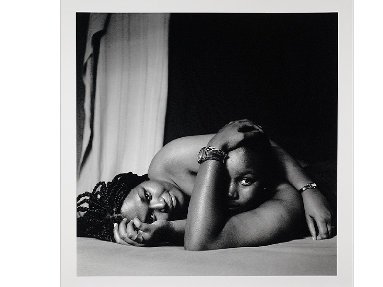 Black and white photo of two women laying down together on a mattress, heads and naked shoulders in view only