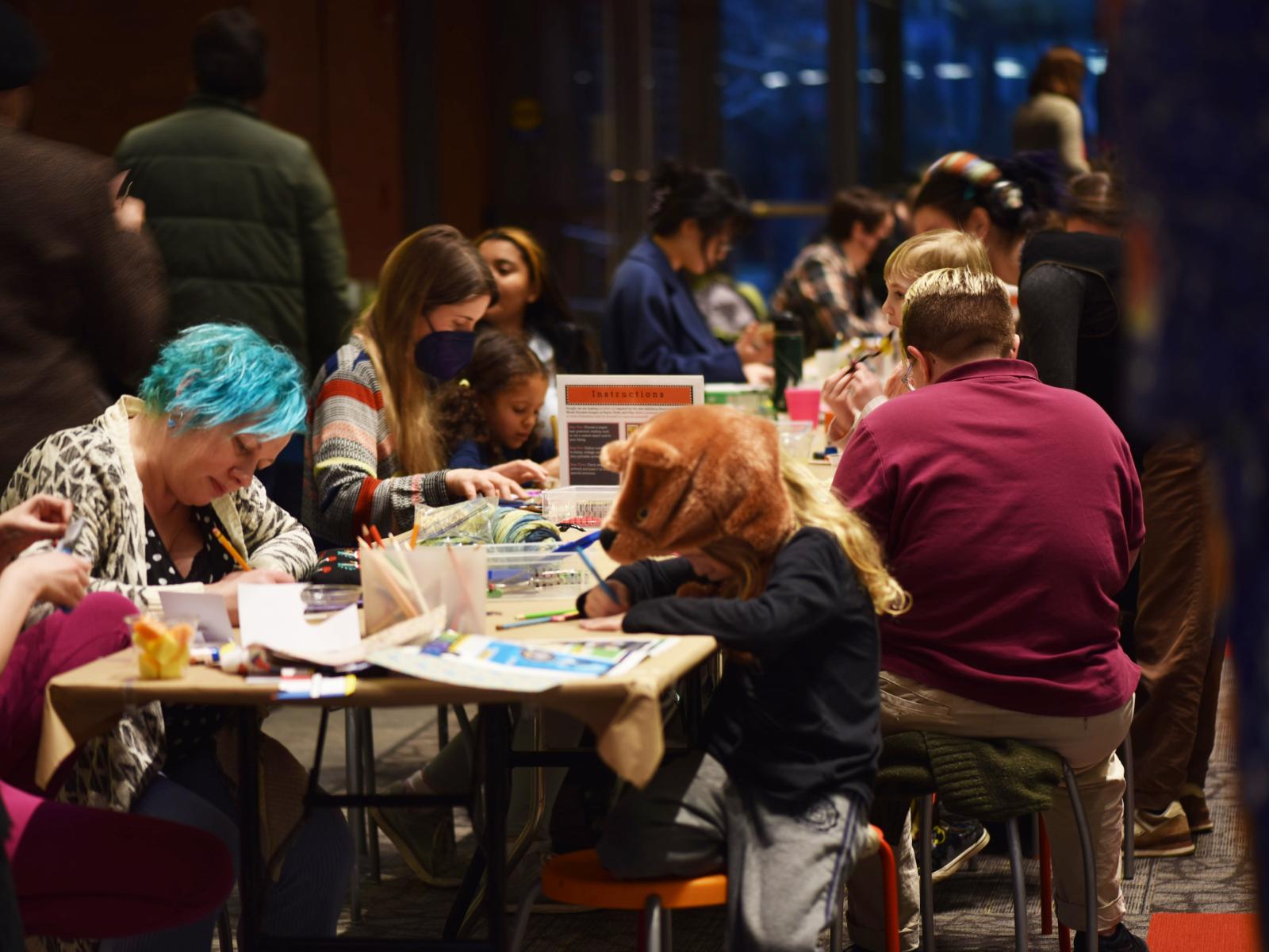 Many people of all ages sitting at a table focussed on making art