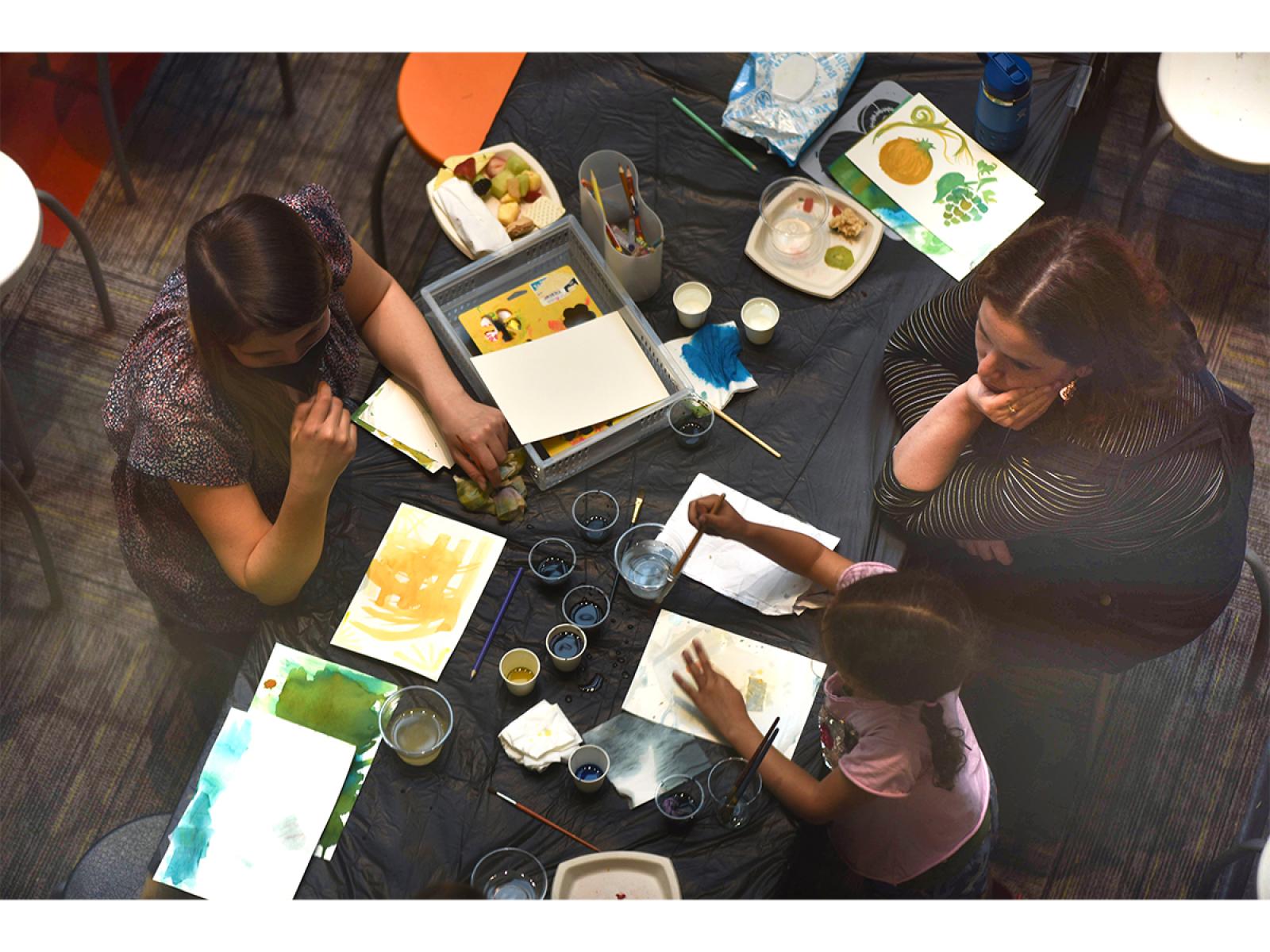 Bird eye view of three Two adults and one child making art at a table.