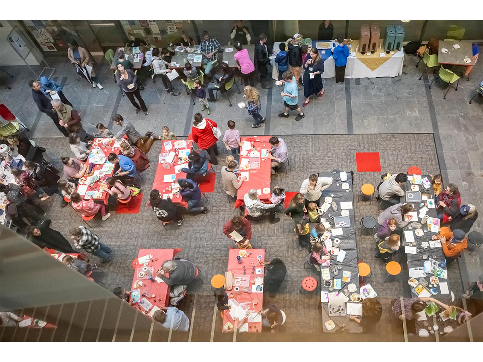 Birds Eye View of people making art at tables and eatng light refreshments together in one high ceilinged room