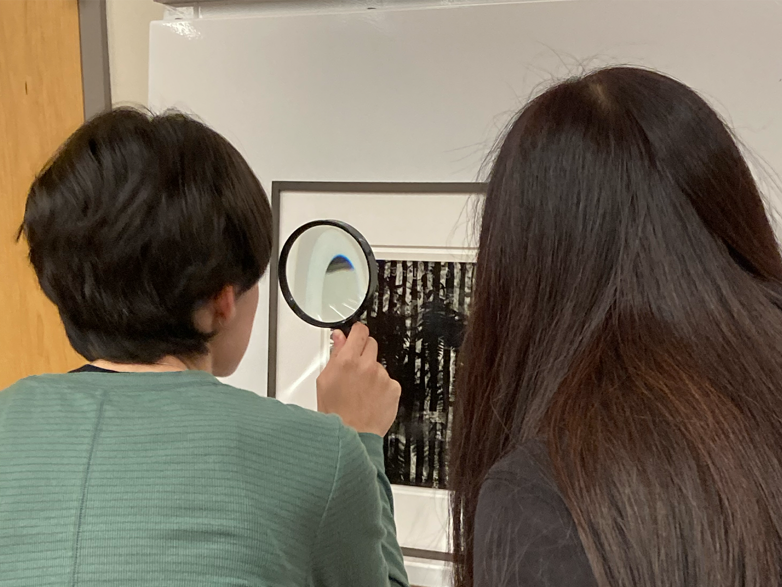 Two people looking at photographs, one with a magnifying glass