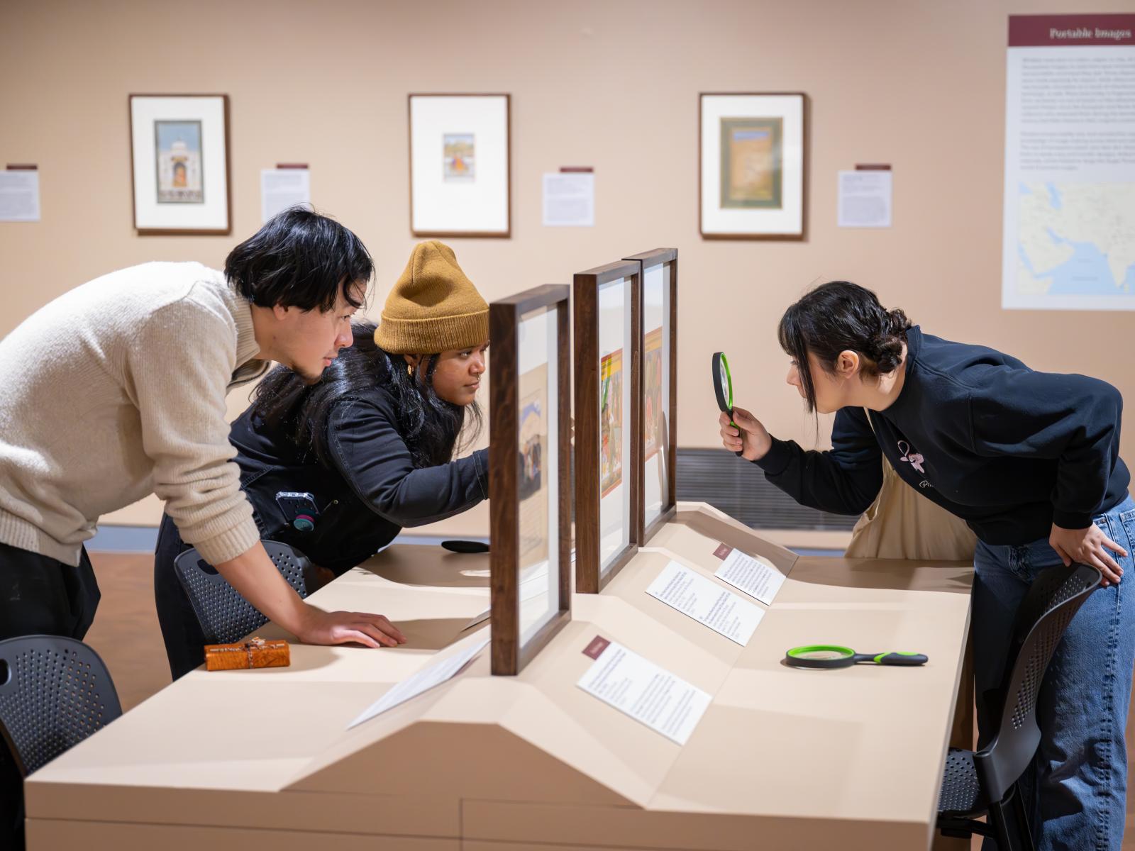 Three people engaging with a work on art closely with magnifying glasses