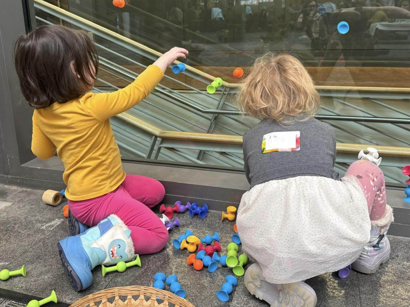Two young people playing with suction cup toys on a glass wall 