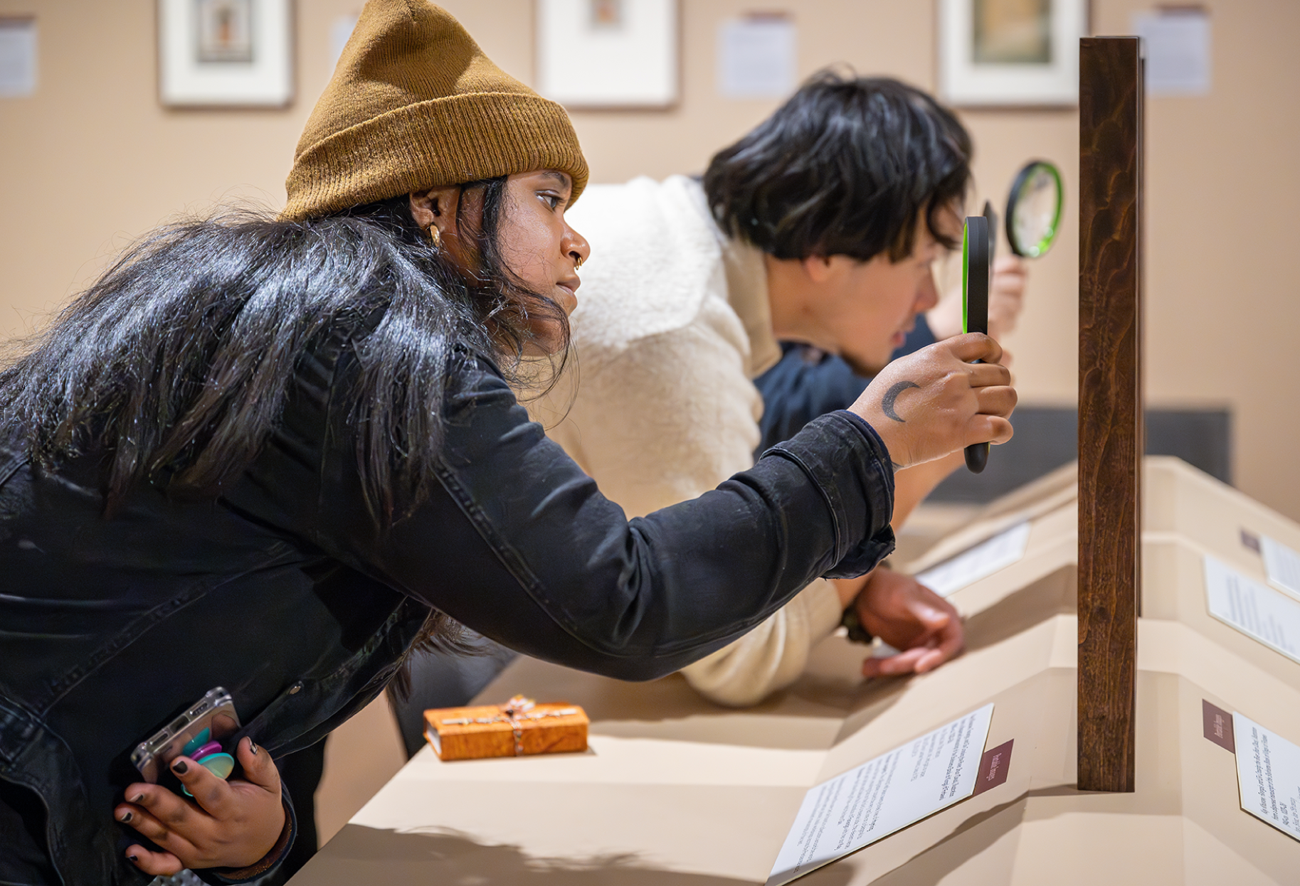 Three students looking closely at art with magnifying glasses