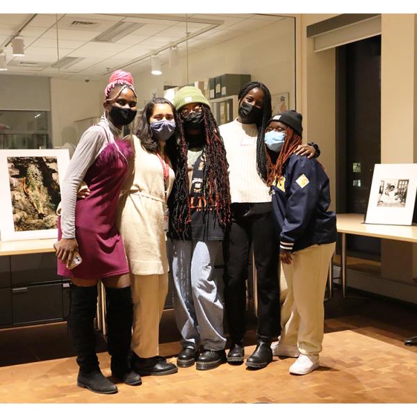 Five students posing for a group picture in the Cunningham Center in front of artwork displayed on a table