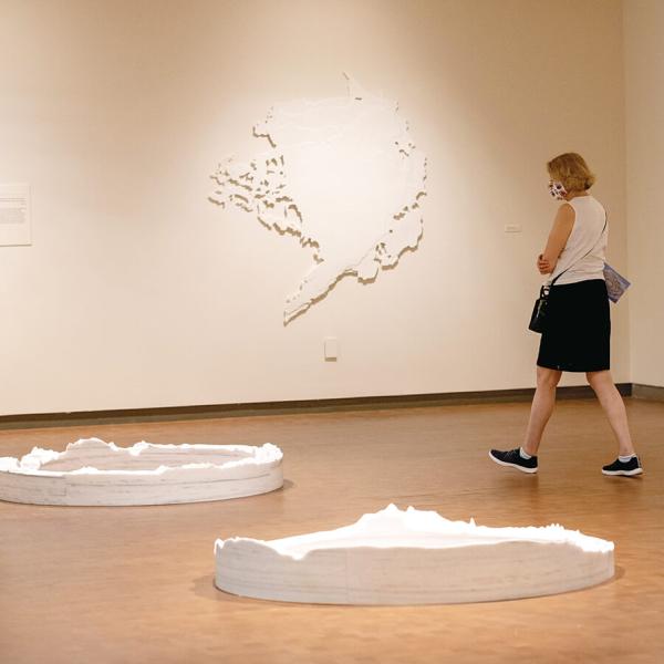 Person in whote blouse and black shorts walking in a gallery with pins on wall and large white circles on the floor