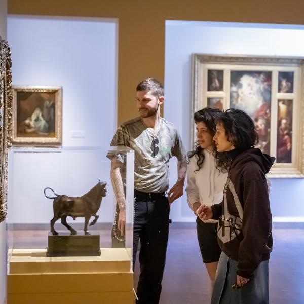 Three young adults in gallery looking at sculpture and paintings