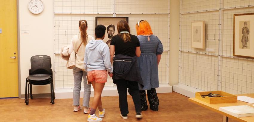 The backs of 5 students looking at art on a wall