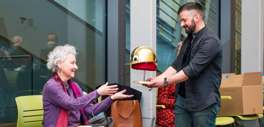 person receiving the gift of a gold hard hat from another person