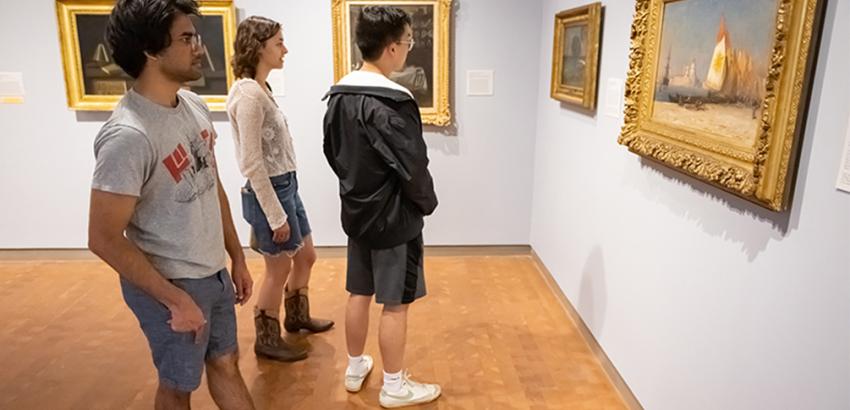 Three young adults in an art gallery looking at paintings on a wall
