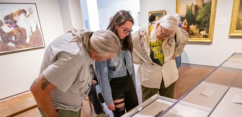 Three people looking at a drawer of works on paper within a gallery