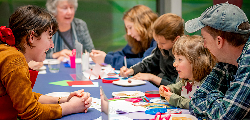 Seven people of various ages sitting around a table talking and making art