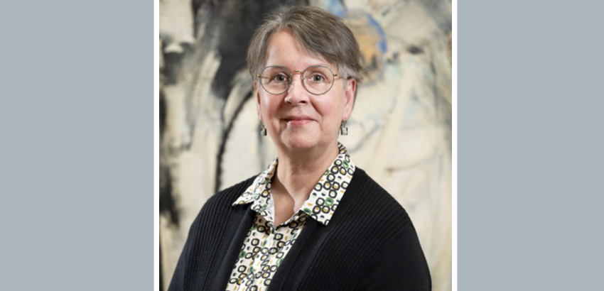 Shoulders up of a person with glasses, short hari and wearing a black sweater standing in front of an abstract painting