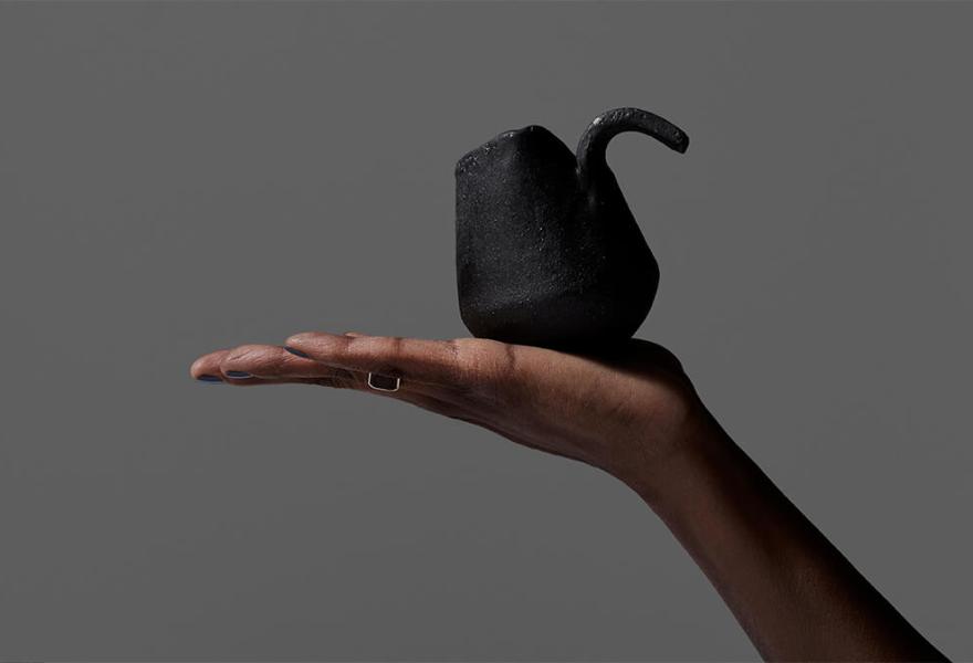 brown skinned hand holding a black ceramic cup with a grey background
