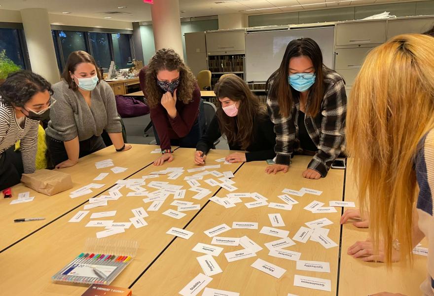 Students in masks standing around a table looking at cut pieces of paper with words on them