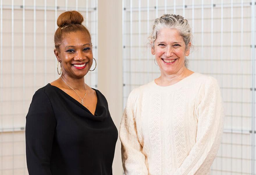 two women smiling, one on left in black sweater and one on right in cream sweater