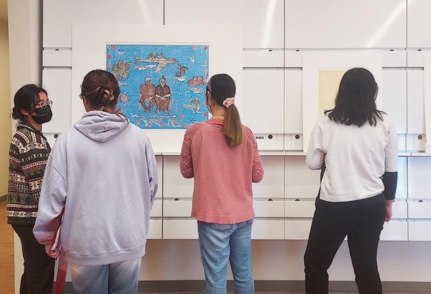 Four students looking at two works on paper lined up on a wall