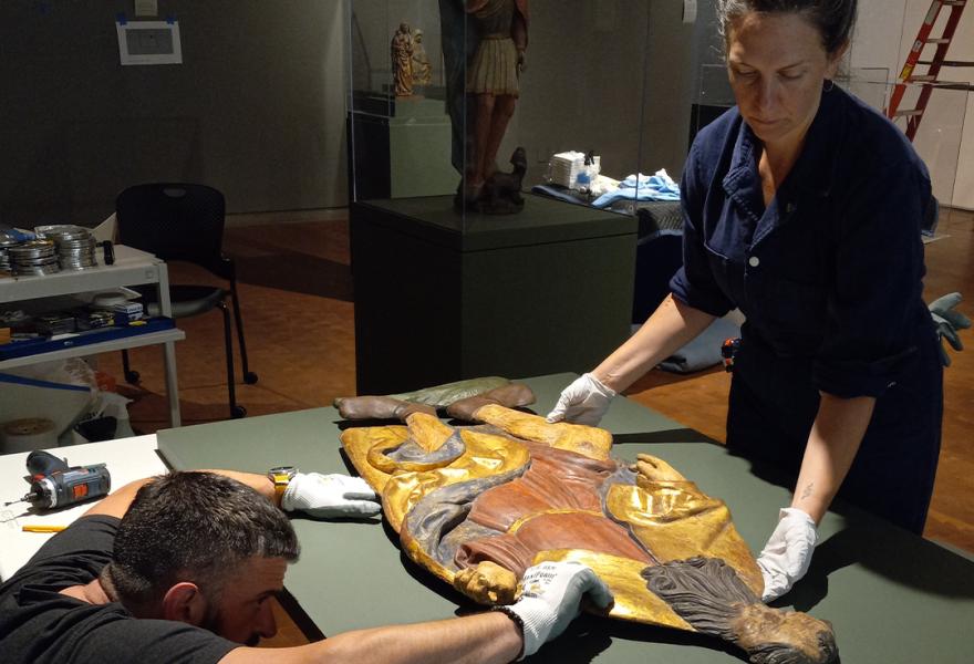 Two people tending to a carved artwork on a table in a gallery