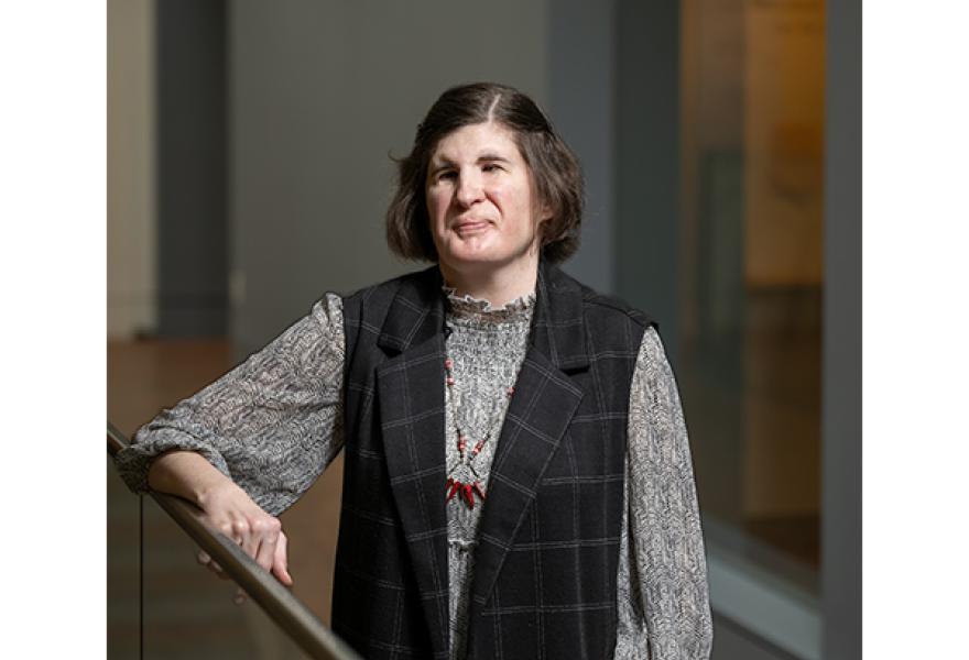 Person with medium brown hair and glasses posing in hallway with arms crossed