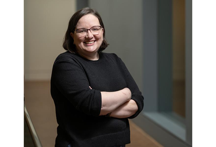 Person with glasses and medium brown hair standing in hallway with arms crossed