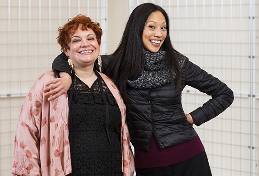 two people smiling and standing together with one on right leaning on the other