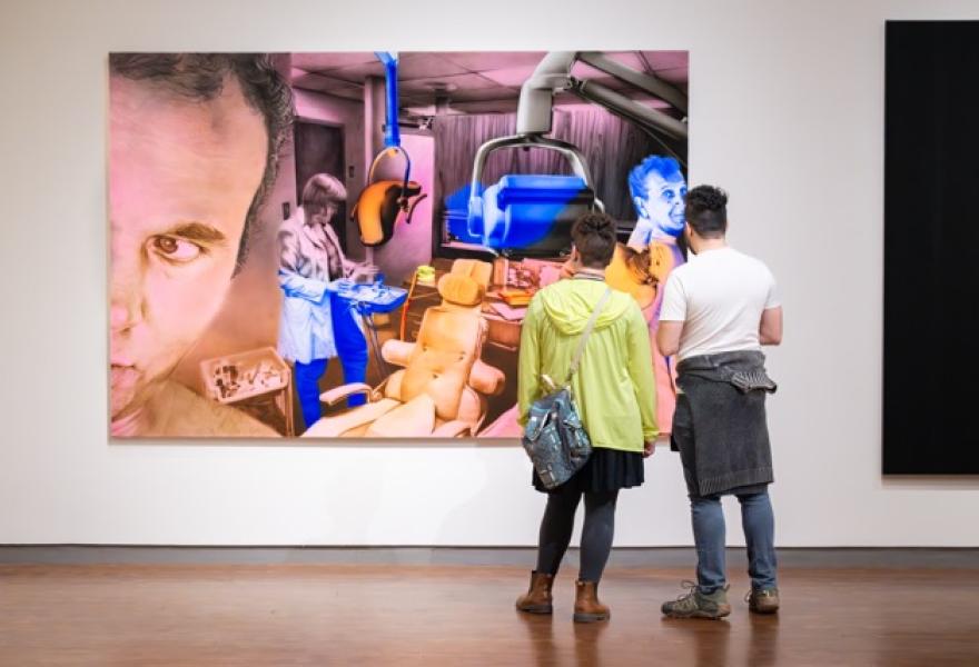 The backs of two people studying a large modern painting in a gallery