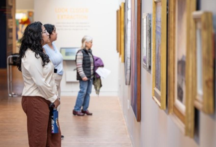 Three visitors looking at paintings on a gallery wall