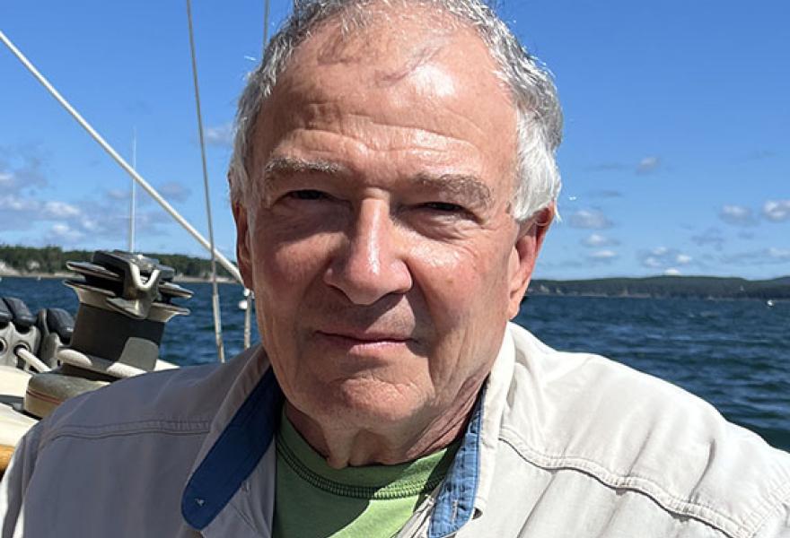 Person with short gray hair in a summer jacket on a boat with the sea in the background