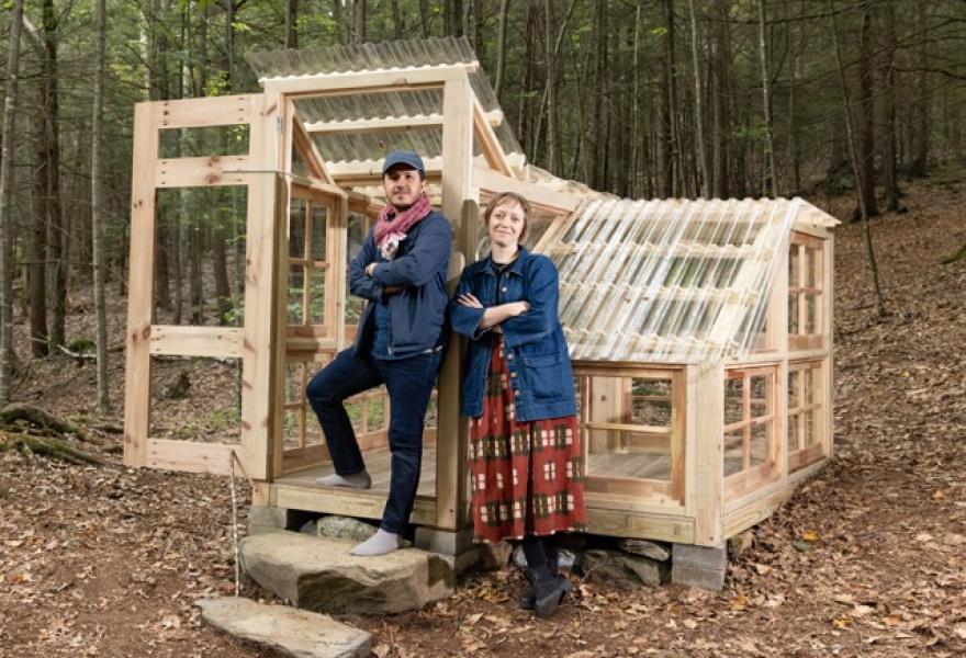Two people standing in front of a wooden structure in the woods