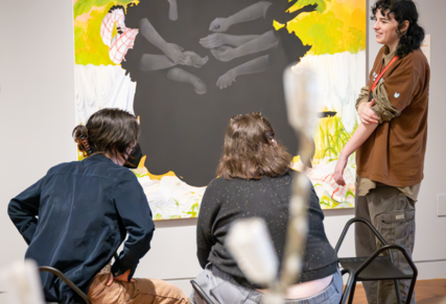 Two people sitting and on standing in conversation front of an abstract artwork on the wall