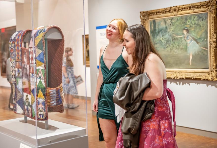 Two women in dresses looking at African beaded art in a gallery