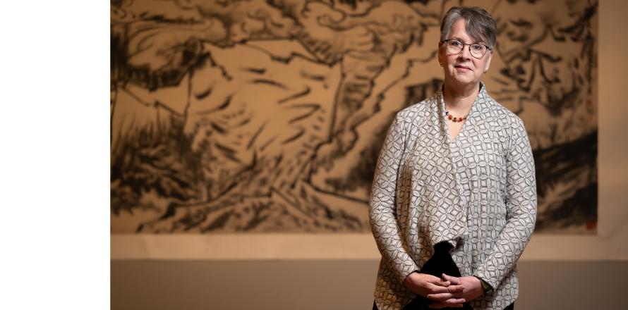 Photo of a woman with short hair standing in front of a calligraphic painting 