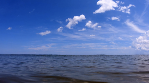 Still from Hopinka's "Cloudless Blue Egress of Summer": slightly cloudy blue sky filling top of frame with ocean water below the horizon line.