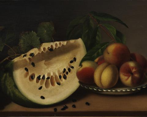A large slice of yellow melon sits next to a pile of peaches. Some of the black seeds have fallen away from the melon and there is foliage behind the fruit. The colors are somber.